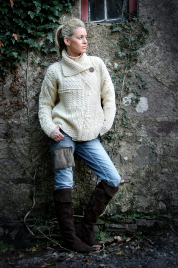 A woman in white sweater and boots leaning against wall.