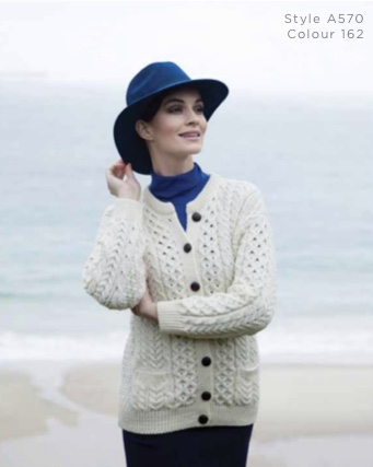 A woman in white sweater and blue hat near the ocean.