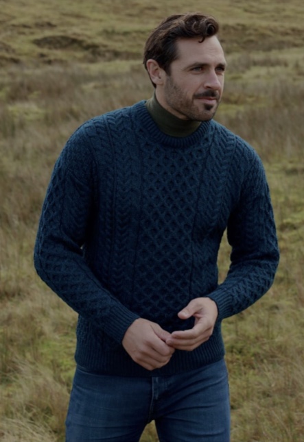 A man in a blue sweater standing on top of a grass covered field.