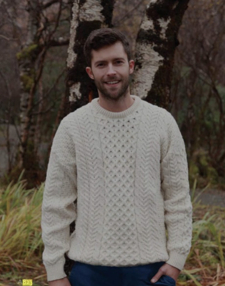 A man in a white sweater standing next to some trees.