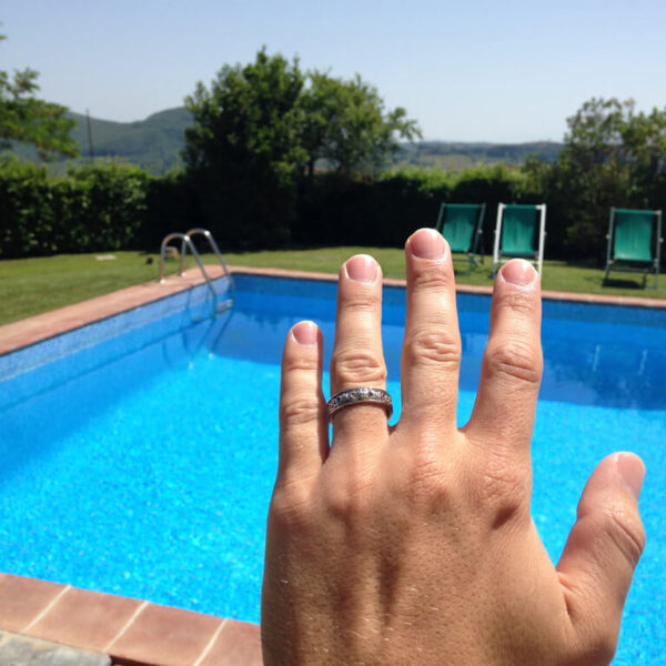 A man is showing off his wedding ring by the pool.