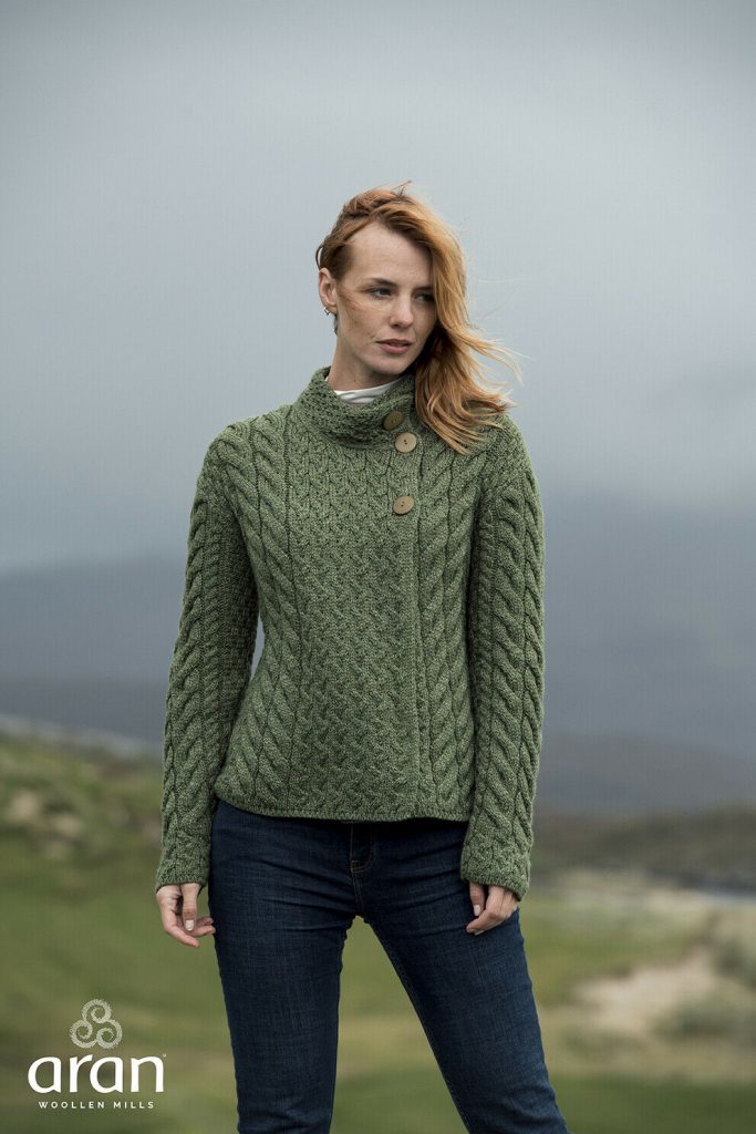 A woman in green sweater standing on top of hill.
