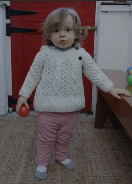 A little girl in pink pants and white sweater holding an apple.