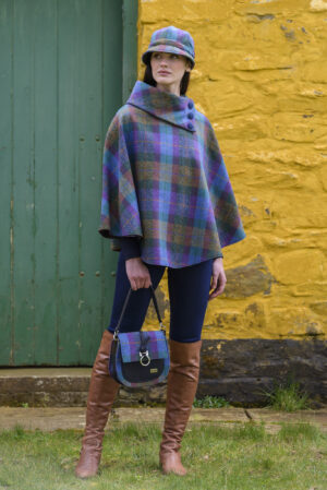 A woman in plaid poncho and boots holding purse.