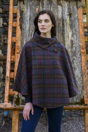 A woman wearing a plaid poncho standing in front of a tree.