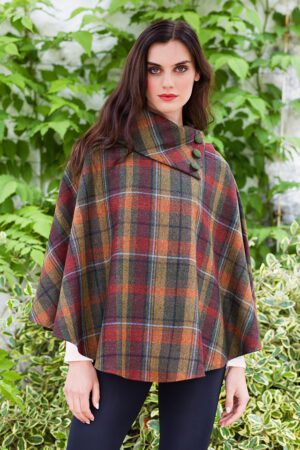 A woman in plaid poncho standing next to bushes.