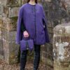 A woman in purple coat and black boots holding a purse.