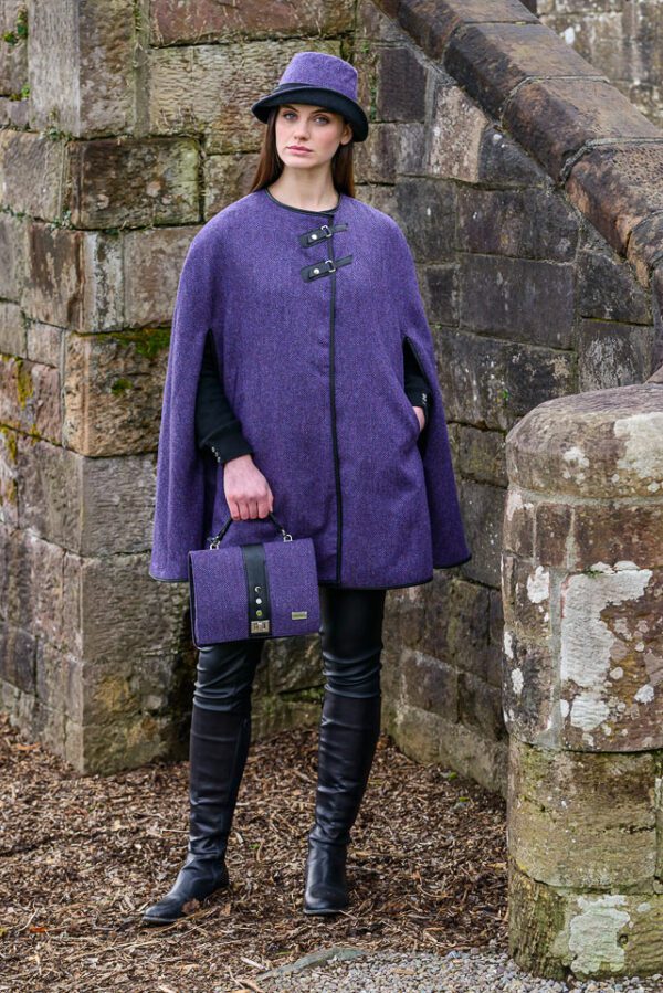 A woman in purple coat and black boots holding a purse.