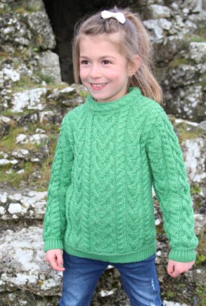 A young girl wearing green sweater standing in front of rocks.