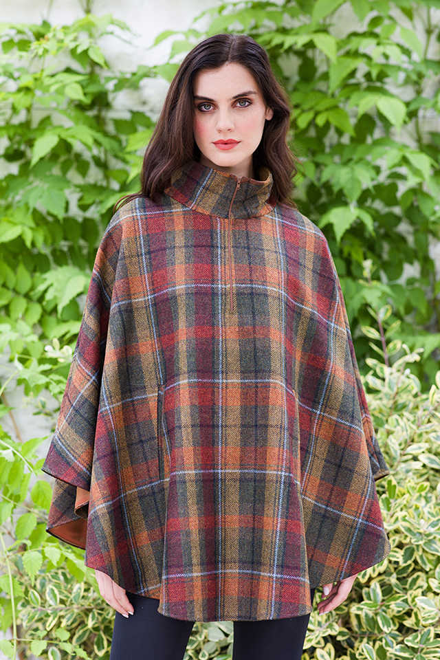 A woman in plaid poncho standing next to tree.