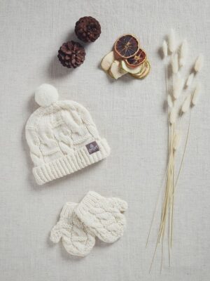 Cozy white knitted hat and mittens with pom-poms on a soft background.