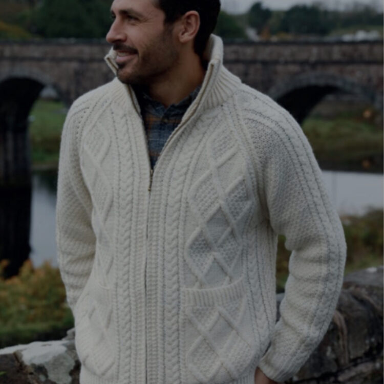A man in a white sweater standing next to a bridge.