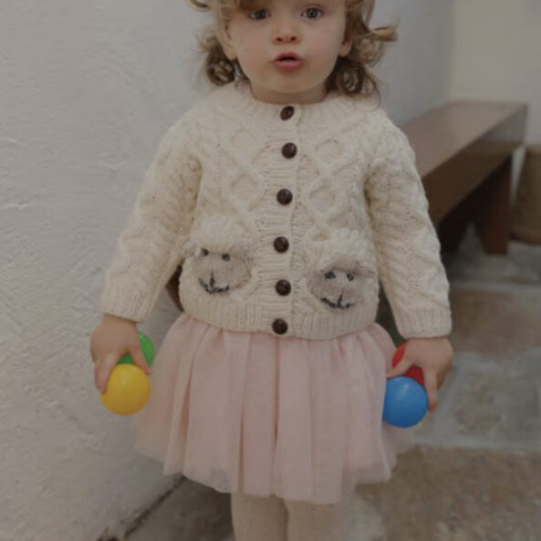 A little girl in a pink skirt holding two eggs.