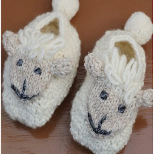 A pair of knitted sheep slippers on top of a wooden table.