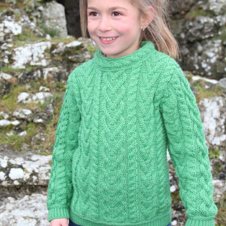 A young girl wearing green sweater standing in front of rocks.