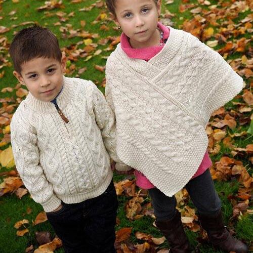 Two children in sweaters standing on a leaf covered lawn.