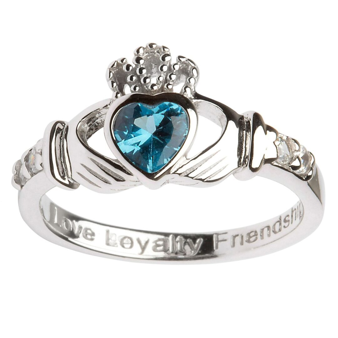 A claddagh ring with blue stone and engraved words.