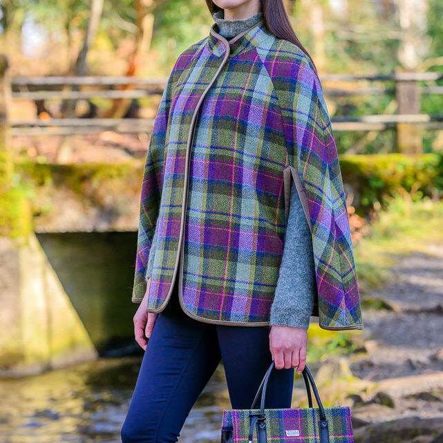 A woman in plaid cape holding a purse.