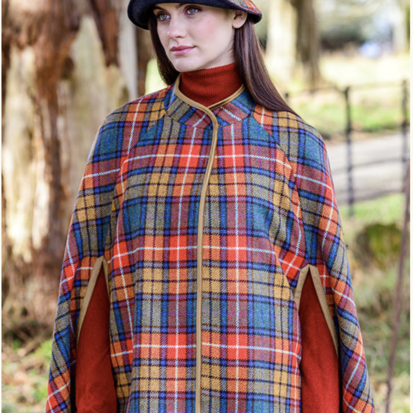 A woman in plaid cape and hat standing outside.