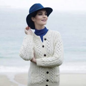 A woman in white sweater and blue hat near the ocean.