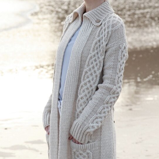 A woman standing on the beach wearing a long cardigan.