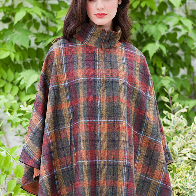 A woman in plaid poncho standing next to tree.