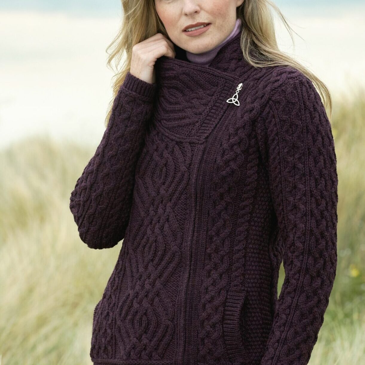 A woman in a purple sweater standing on top of a beach.