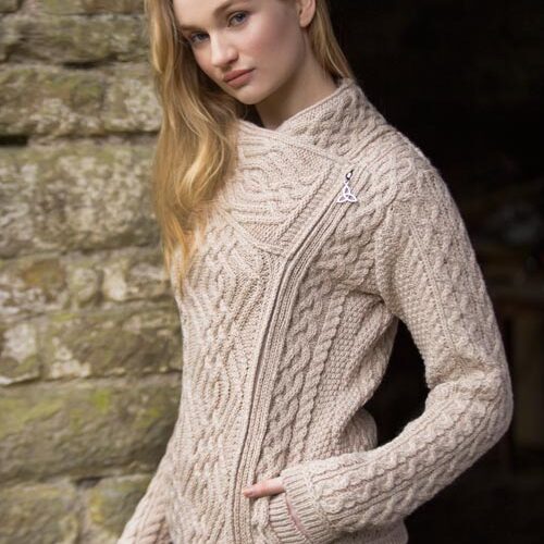 A woman in a beige sweater standing next to a stone wall.