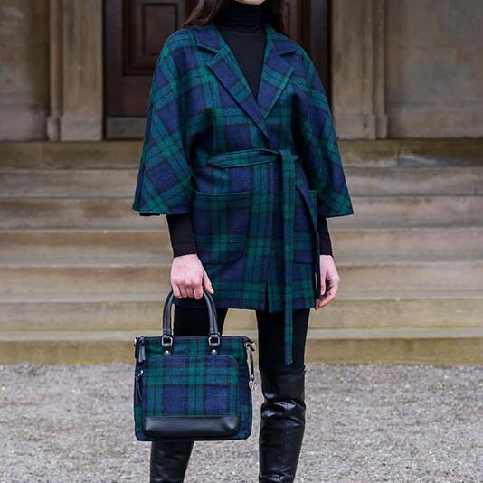 A woman in black and green plaid coat holding a purse.