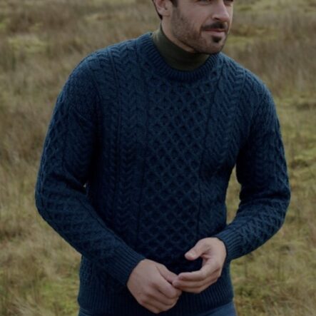 A man in a blue sweater standing on top of a grass covered field.