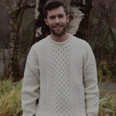 A man in a white sweater standing next to some trees.